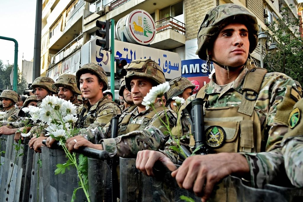 Lebanese army soldiers carry flowers offered to them by a supporter of outgoing Lebanese premier Saad Hariri during a protest in Beirut's Corniche al-Mazraa neighbourhood on December 20, 2019. Anger was fuelled among members of Lebanon's Sunni community who said the prime-minister-designate did not enjoy the sect's backing for a post reserved for Sunni Muslims by a power-sharing system enshrined after the end of the 1975-1990 civil war. / AFP / -