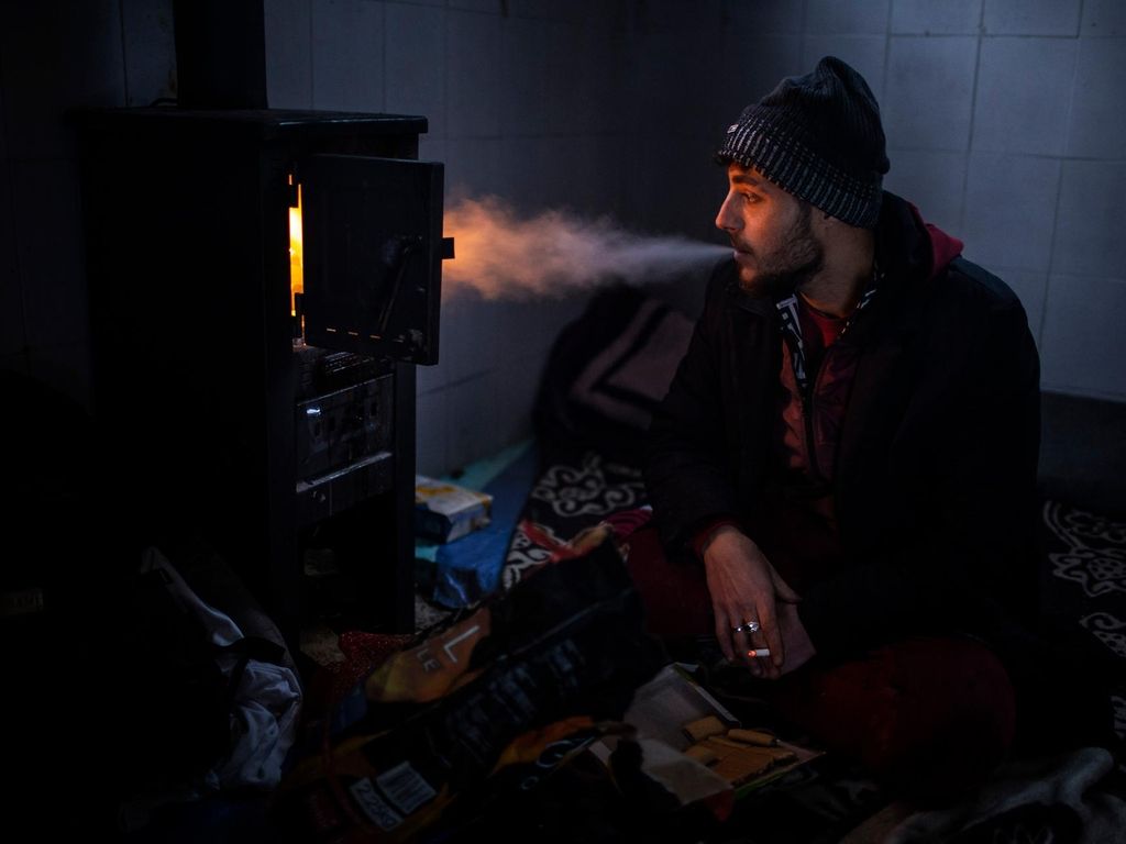 Yousef, 27, smokes a cigarette in front of the stove inside a cabin that he uses to sleep during his journey through the mountains of Bosnia to cross the border. JM Lopez / The National