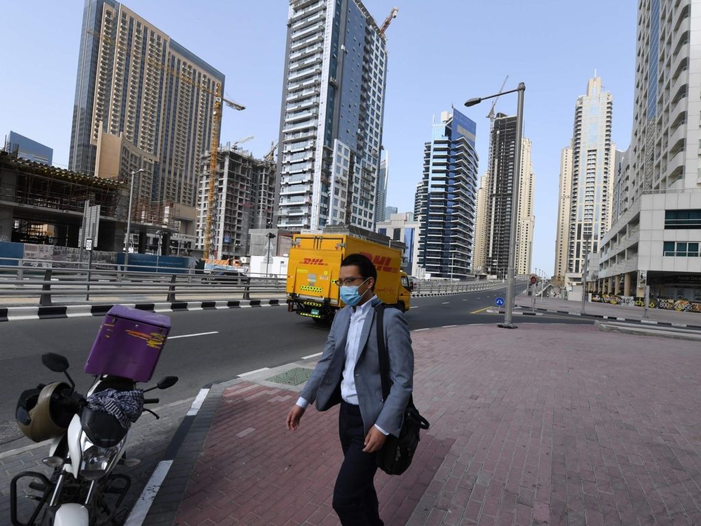 A man, wearing a protective mask, walks down the street in Dubai on March 16, 2020. No shisha pipe sessions, deserted streets, mosques and shopping malls, drones in the sky broadcasting public health warnings -- the new coronavirus has turned life upside down in Gulf societies. / AFP / KARIM SAHIB