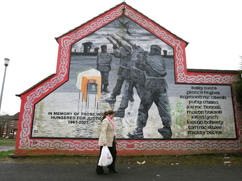 A woman walks past an old IRA Hunger Strike mural west Belfast, Northern Ireland. Photo/Paul McErlane