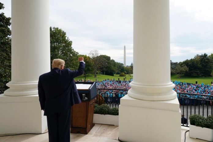 President Donald Trump gestures from the balcony of the Blue Room of the White House