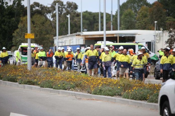 Construction workers in high visibility clothing and hard hats walk from Curtin University after a roof collapse.