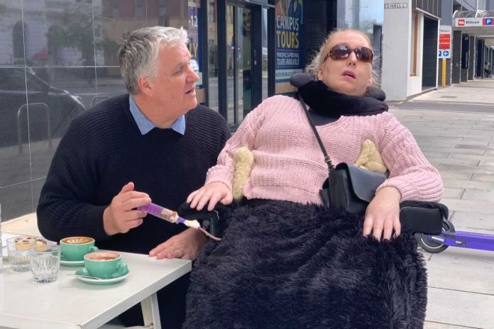 A carer helps feed a woman with a disability.