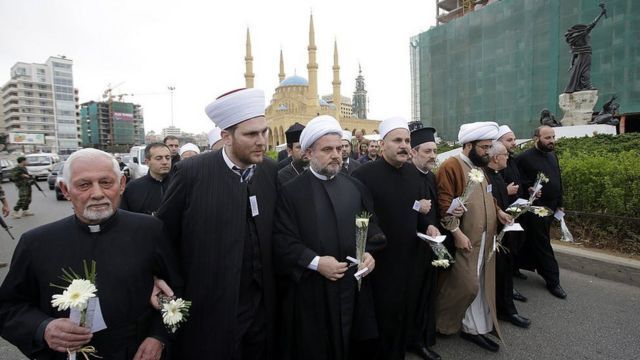 Clerics distribute white flowers to citizens on the anniversary of the 2013 civil war