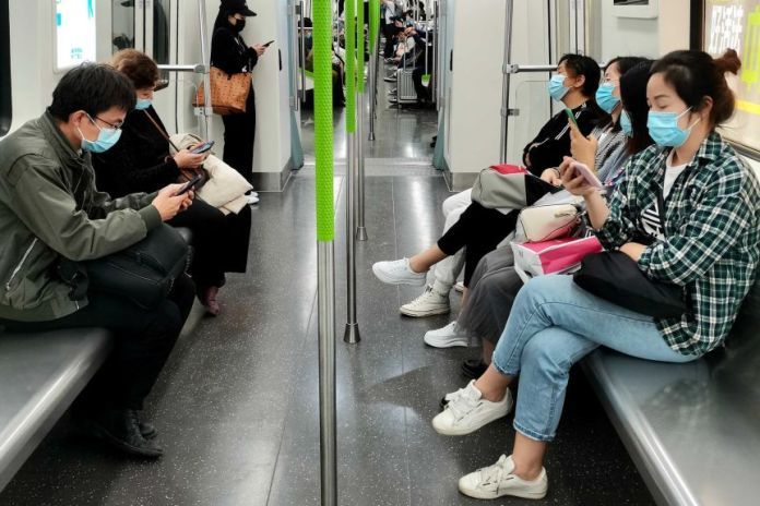 People sitting on a subway wearing masks and looking at phones.