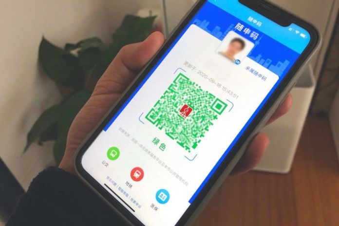 You see a hand holding a smartphone close-up with a green QR code in the center of the screen against a blue background.