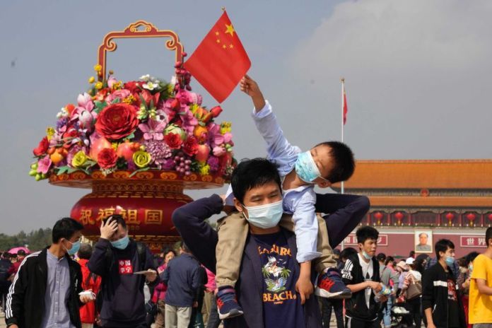 Tourists wearing masks to protect themselves from the coronavirus stand near a flower decoration.
