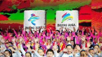 People appear in colorful outfits in front of the Beijing 2022 banners.