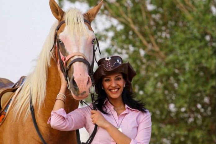 A woman in a pink shirt and cowboy hat smiling next to a horse