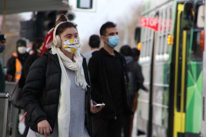 A person wearing a lemon print face mask walks towards a tram.