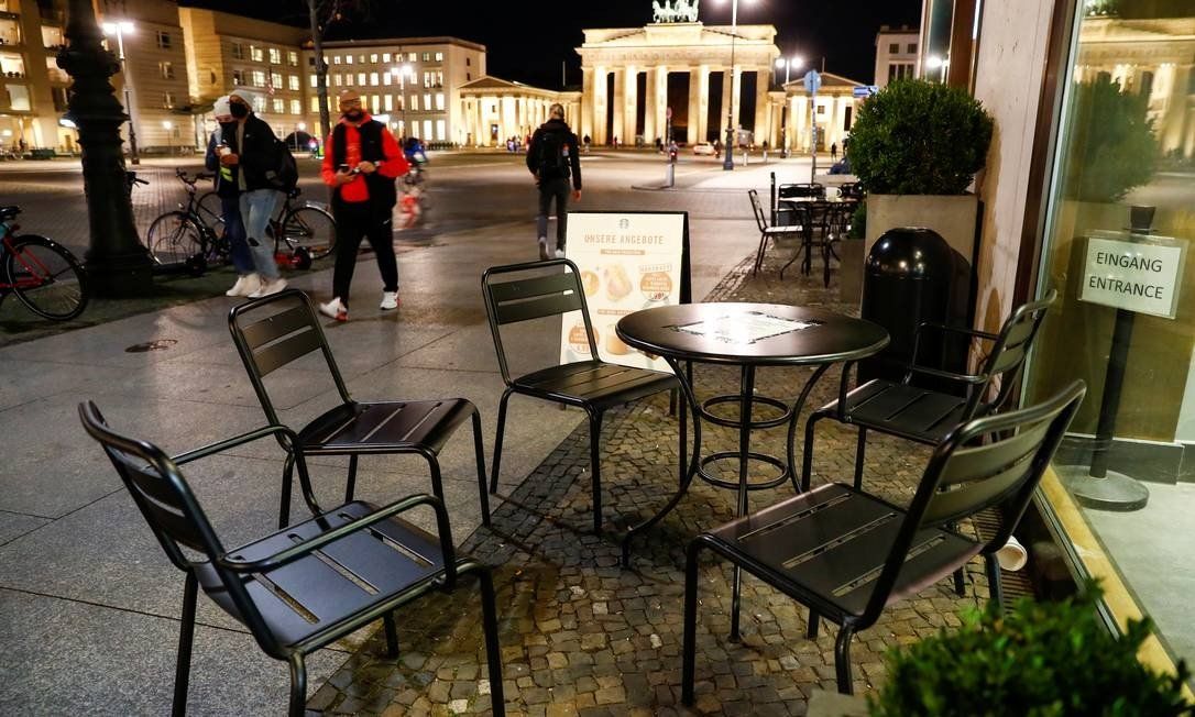 Pedestrians pass empty cafe tables in front of the Brandenburg Gate in Berlin, Germany. The country's government decided on Wednesday (28) to enact a partial quarantine starting on November 2 Photo: FABRIZIO BENSCH / REUTERS