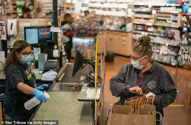 About 75% had no symptoms and workers who dealt with customers were five times more likely to test positive. Pictured: Cindy Lambing completes her purchases at Linden Hills Coop as cashier Sareena Tippett cleans up the Minnesota till in May 2020