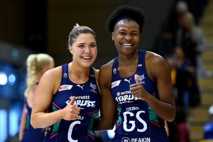 Two Melbourne Vixens super netball players smile as they celebrate as they beat the Giants.