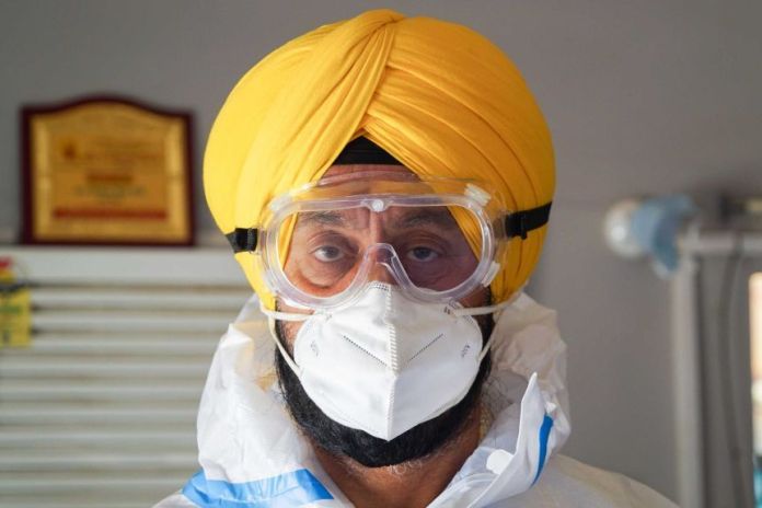 A Sikh man in a yellow turban and full PPE with goggles and mask