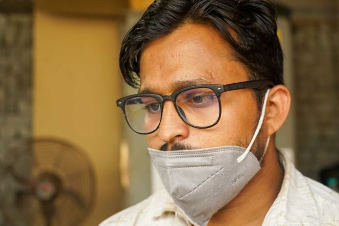 A young man in glasses with a face mask over his mouth that looks somber