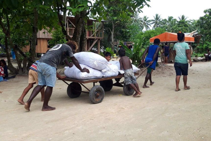 Locals, including children, work together to push a buggy loaded with sacks of goods.