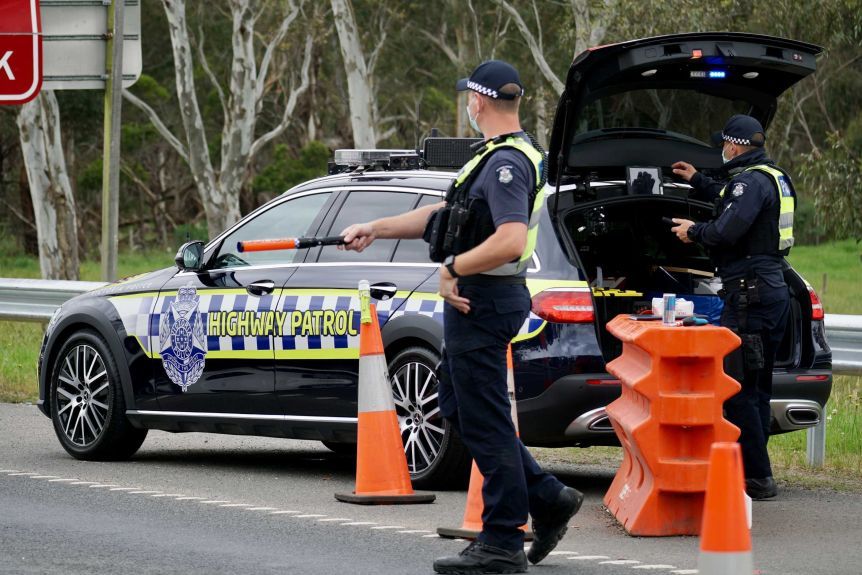 A police officer stands next to a police car that directs traffic at a checkpoint.