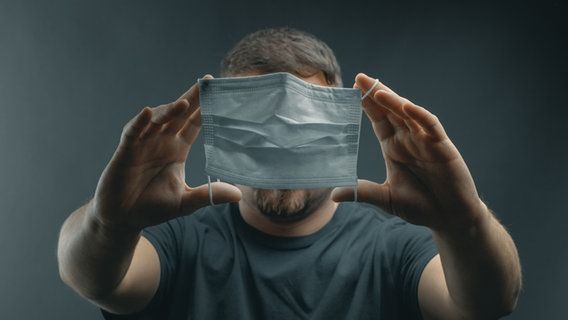 A man holds a mask in front of his face. © Brilliant Eye / photocase.de Photo: Brilliant Eye / photocase.de