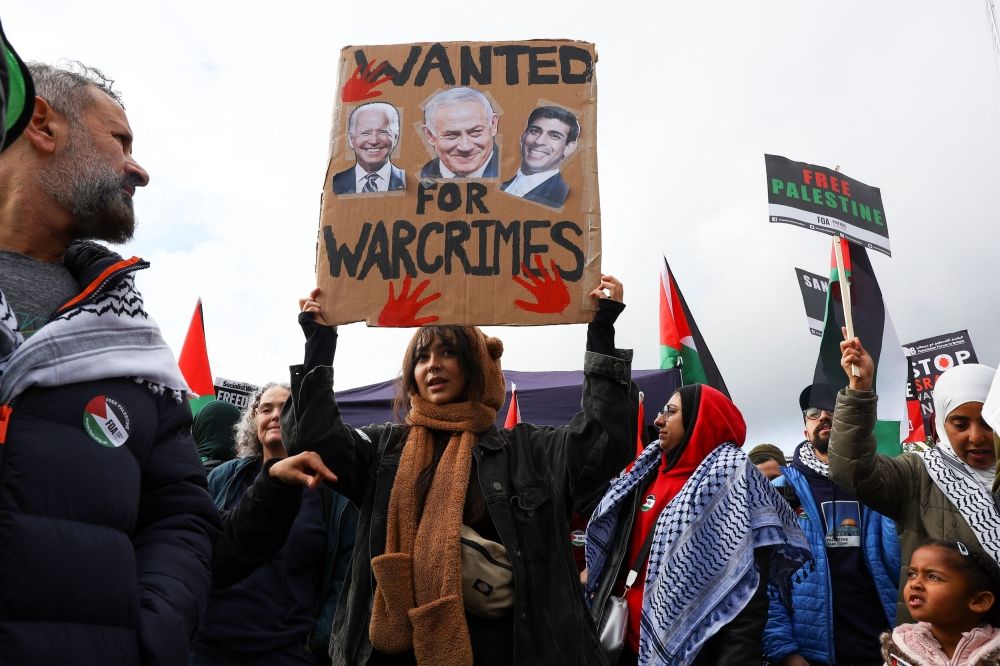 A demonstrator holds up a sign featuring images of US President Joe Biden, Israeli Prime Minister Benjamin Netanyahu and British Prime Minister Rishi Sunak, at a protest in solidarity with Palestinians in Gaza, amid the ongoing conflict between Israel and the Palestinian Islamist group Hamas, in London, Britain, October 21, 2023. — Reuters pic
