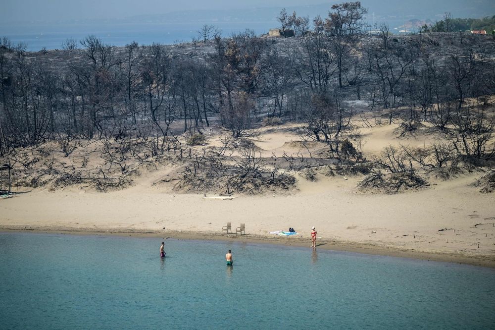 A woman enters the sea from a beach where wildfires destroyed the woods, at Glystra near the village of Gennadi in the southern part of the Greek island of Rhodes, on July 27, 2023. Last month smashed the previous November heat record, pushing 2023’s global average temperature to 1.46 degrees Celsius warmer than pre-industrial levels, the EU’s Copernicus Climate Change Service said. — AFP pic