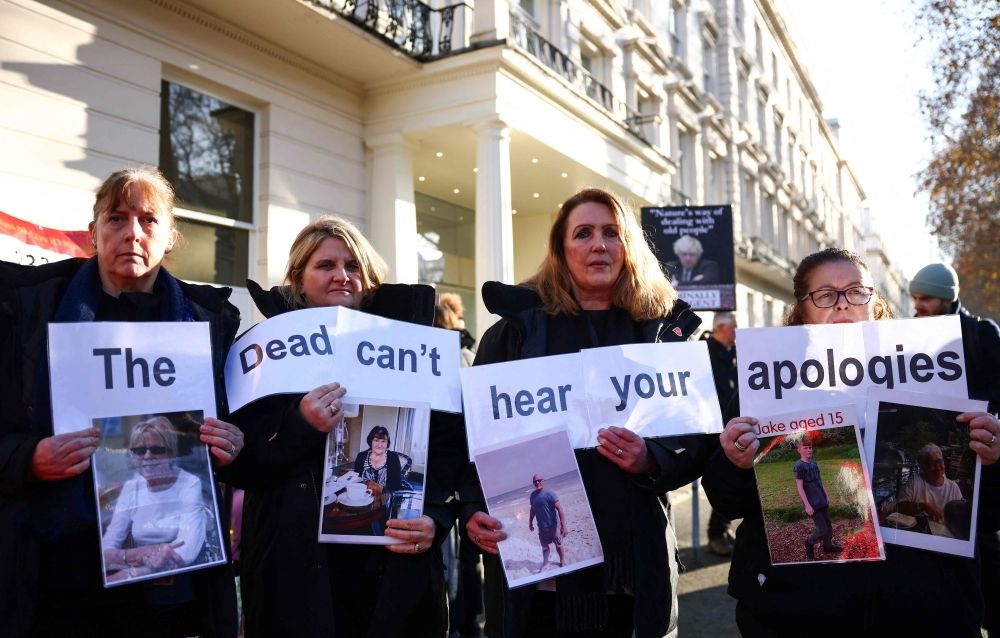 Protesters holds a placard reading ‘The dead can't hear your apologies’ duing a gathering outside the UK Covid-19 Inquiry building in west London, on December 6, 2023 as Britain's former Prime Minister Boris Johnson is inside giving evidence regarding his management of the pandemic.