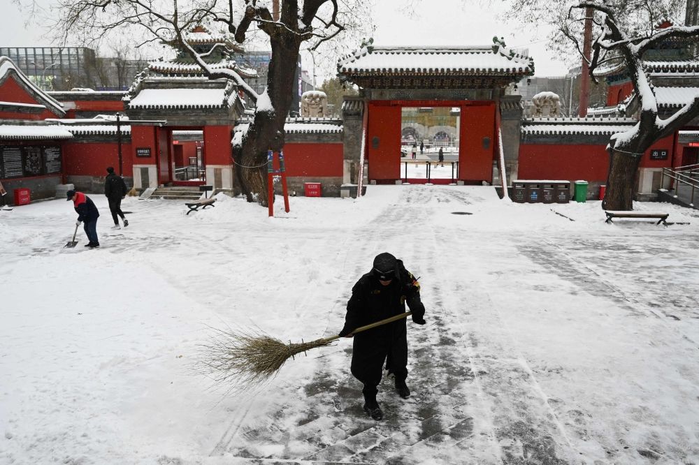 A worker sweeps a walkway in a temple during a snowfall in Beijing December 14, 2023. — AFP pic