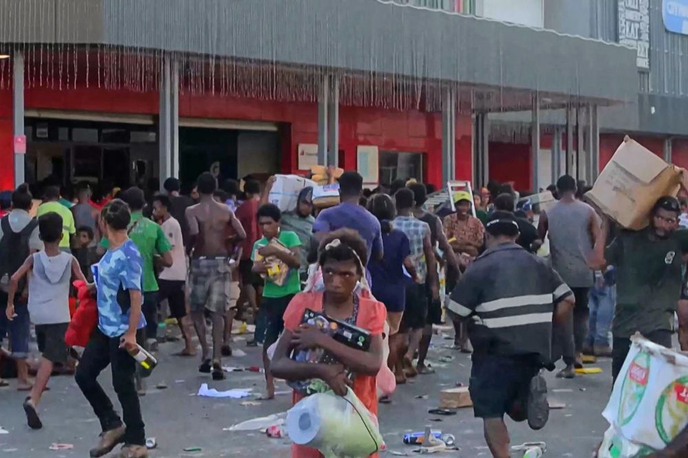 This screen grab from AFPTV video footage taken on January 10, 2024 shows people carrying items as crowds leave shops with looted goods amid a state of unrest in Port Moresby. — AFP pic