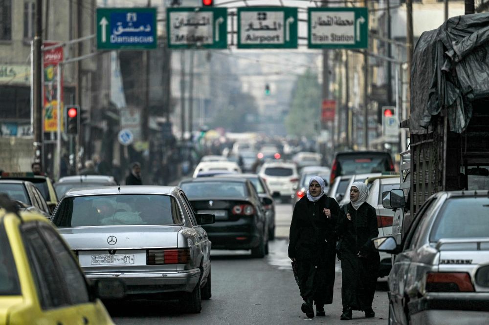 Two women walk past moving vehicles along a street in Syria's northern city of Aleppo on December 11, 2024. Islamist-led rebels took the Syrian capital Damascus in a lightning offensive on December 8, ousting president Bashar al-Assad and ending five decades of Baath rule in the country. — AFP pic