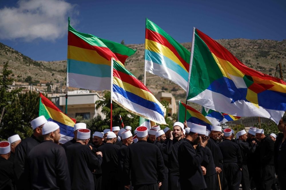 Who are the Druze, the secretive Syrian Muslim sect dragged into conflict amid regime change and Israeli attacks? Druze men lift their flags as they await the arrival of Syrian Druze clerics in a bus through a border barrier guarded by Israeli soldiers, in the village of Majdal Shams in the Israeli-annexed Golan Heights, on April 25, 2025. — AFP pic