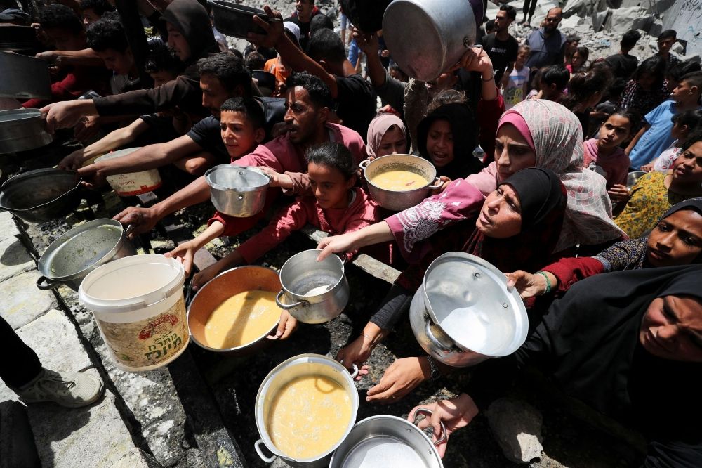 Palestinians wait to receive food cooked by a charity kitchen, in Jabalia, in the northern Gaza Strip, May 19, 2025. — Reuters pic