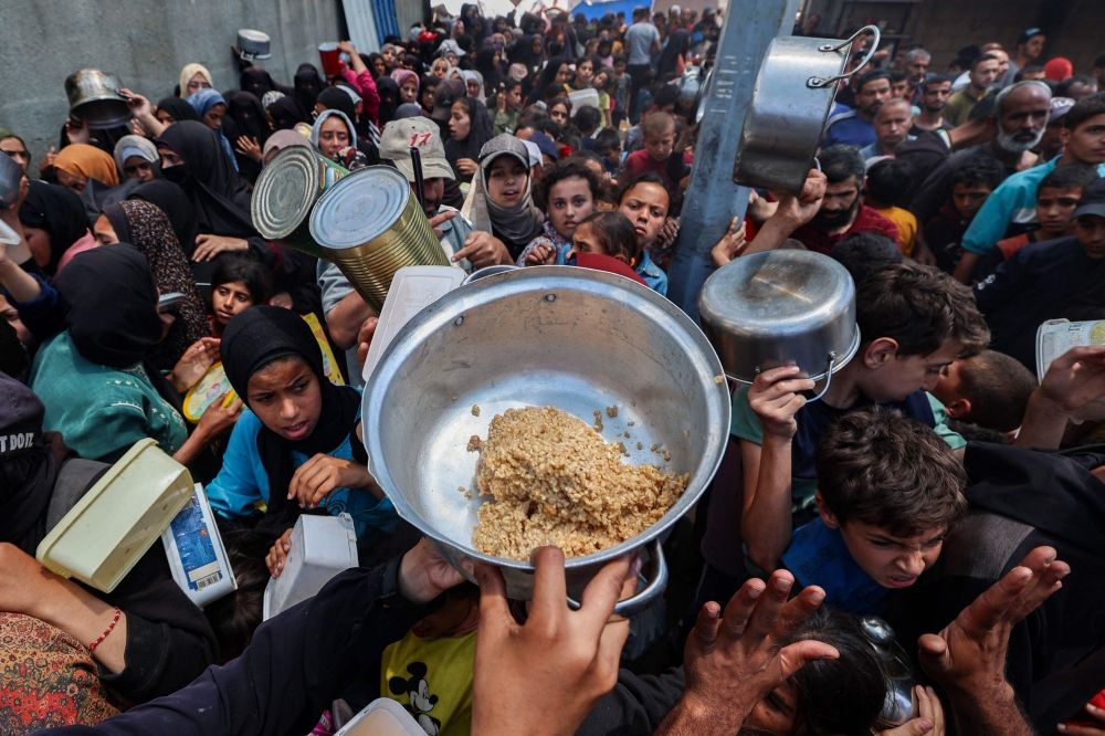 Palestinians gather to receive a hot meal at a food distribution point in the Nuseirat camp for refugees in the central Gaza Strip on May 21, 2025. — AFP pic