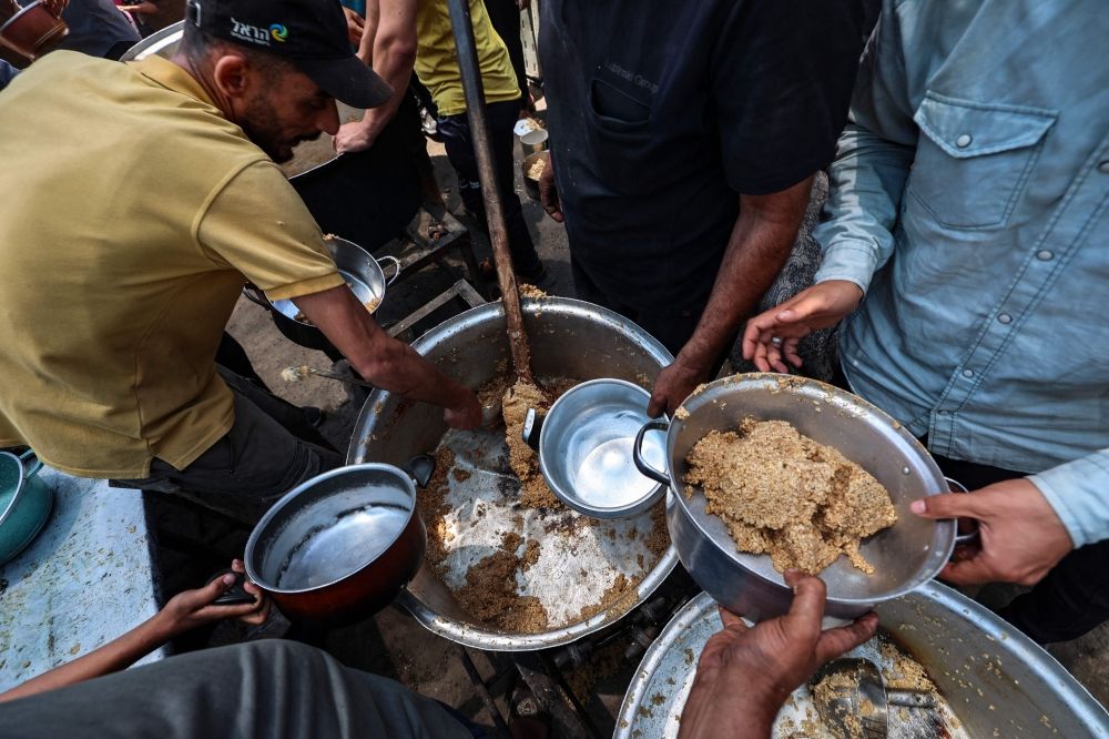 Volunteers distribute hot meals in the Nuseirat camp for refugees in the central Gaza Strip on May 21, 2025. Gazans waited desperately for vital supplies on May 21 after Israel said it let in dozens of UN trucks but faced mounting international pressure to increase the aid flow and abandon its intensified military campaign. — AFP pic