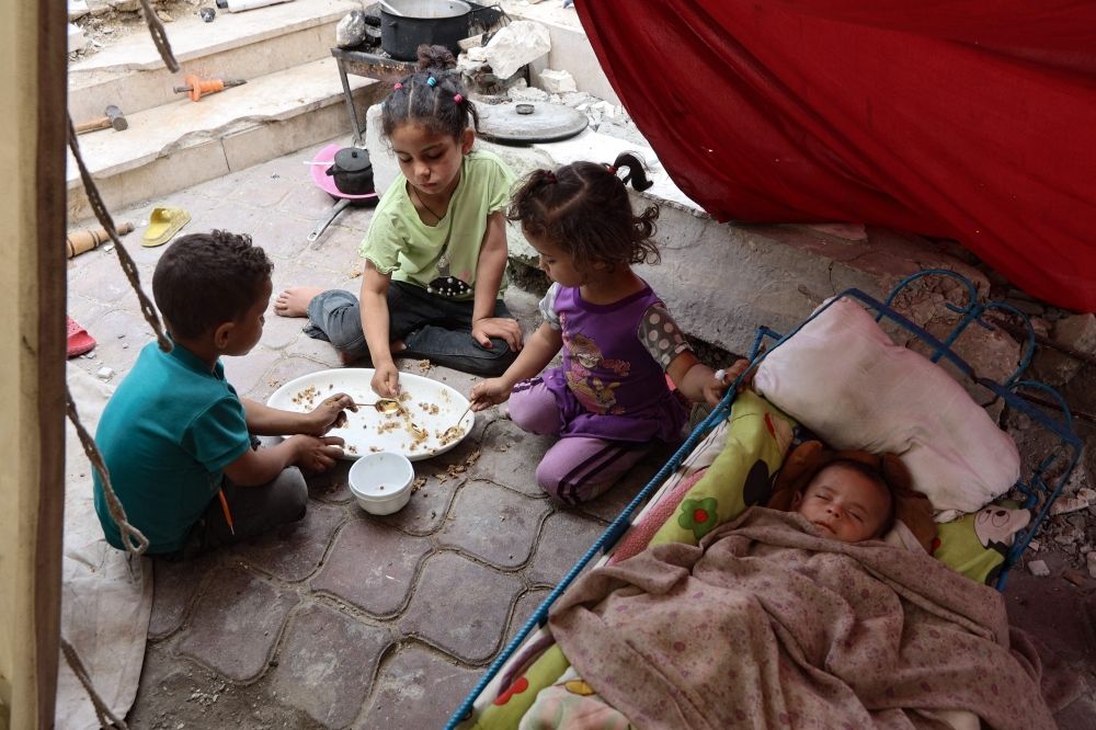 Palestinian children share a meal of rice as a baby sleeps, inside a tent at a displacement camp near Gaza City's port May 22, 2025. — AFP pic