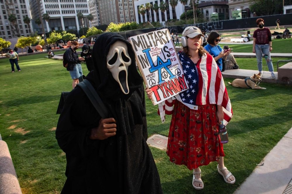 Trump slams protesters as ‘animals’, White House blames California leaders for escalating unrest A person wears a 'Ghostface' mask next to another holding a sign as they gather at Pershing Square to protest against federal immigration operations in downtown Los Angeles yesterday. — AFP pic