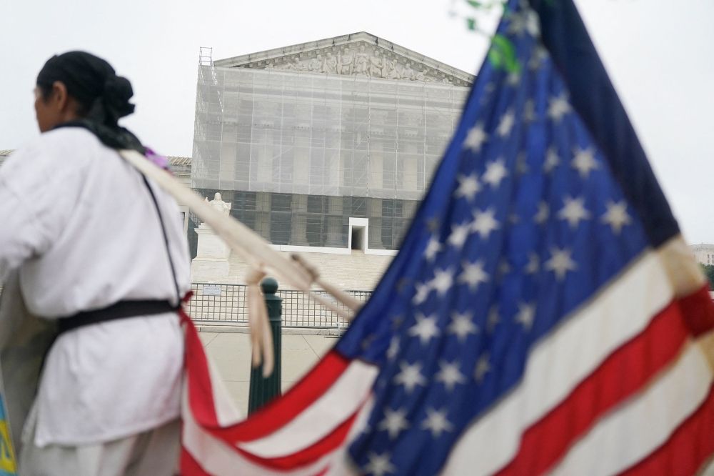 A person stands with a US flag attached to them, after the US Supreme Court dealt a blow to the power of federal judges by restricting their ability to grant broad legal relief in cases as the justices acted in a legal fight over President Donald Trump’s bid to limit birthright citizenship, outside the court in Washington, D.C.June 27, 2025. — Reuters pic