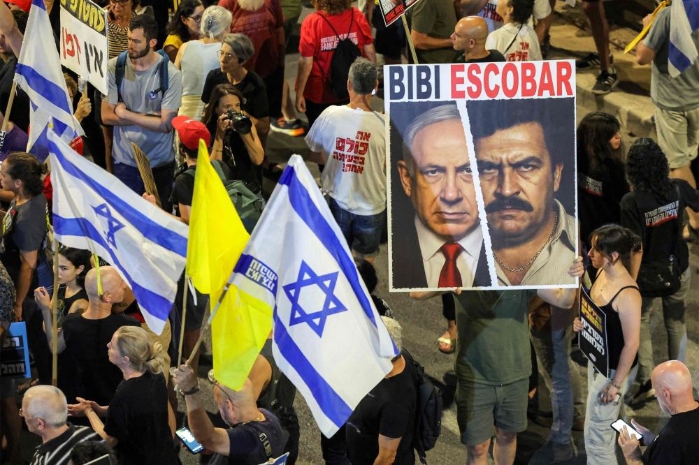 ‘Terrible failures’: Netanyahu’s Iran lustre fades, comes under fire at home as pressure grows to end Gaza war A demonstrator holds a sign depicting a mashup of the faces of Israeli Prime Minister Benjamin Netanyahu and late Colombian drug lord Pablo Escobar during an anti-government protest outside the Israeli Defence Ministry headquarters in Tel Aviv on June 28, 2025. — AFP pic