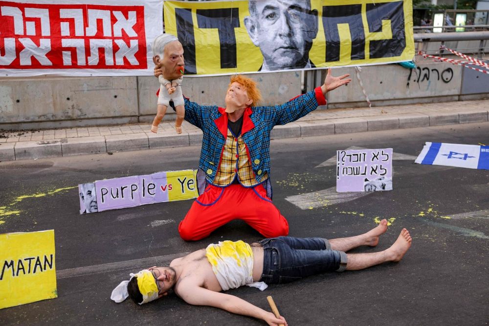 A demonstrator in a clown costume with a mask depicting US President Donald Trump holds a baby puppet depicting Israel's Prime Minister Benjamin Netanyahu next to a man lying on the ground depicting an Israeli hostage. — AFP pic