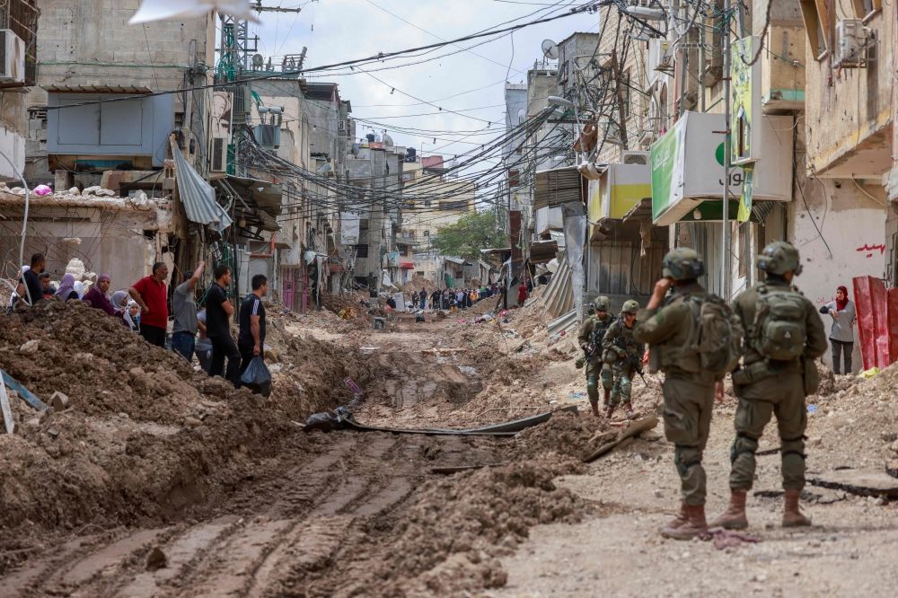 Israeli soldiers look on as Palestinians carry their belongings after being ordered to leave their homes during an Israeli operation in the Tulkarem camp for refugees in the north-west of the occupied West Bank May 2, 2025. — AFP pic