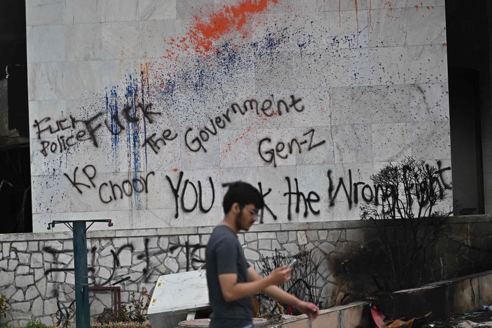 A man uses a phone as he walks past a graffitied wall on the facade of the torched Parliament building in Kathmandu on September 14, 2025. — AFP pic A man uses a phone as he walks past a graffitied wall on the facade of the torched Parliament building in Kathmandu on September 14, 2025. — AFP pic