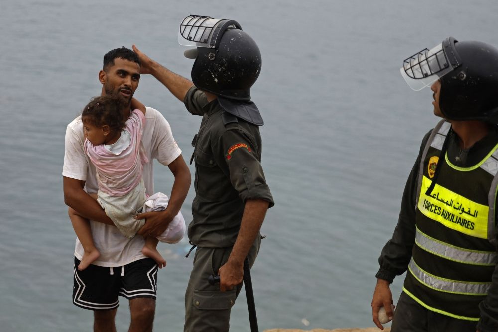 Hundreds of unaccompanied minors endure harsh conditions in Ceuta migrant influx A member of Moroccan security forces gestures to a man carrying a child close to the site of clashes near Fnideq, on the Morocco-Spain border July 31, 2026. Hundreds of unaccompanied minors slept outdoors in a disused industrial park in Ceuta after swimming to the Spanish territory from Morocco. — AFP pic